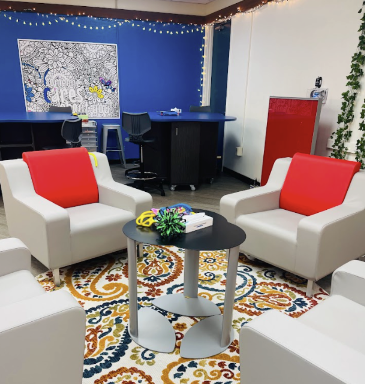 A classroom with blue walls, grey arm chairs, and red pillows on each arm chair.