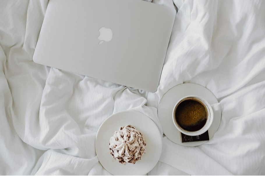 Laptop, a cupcake and a book on white sheets