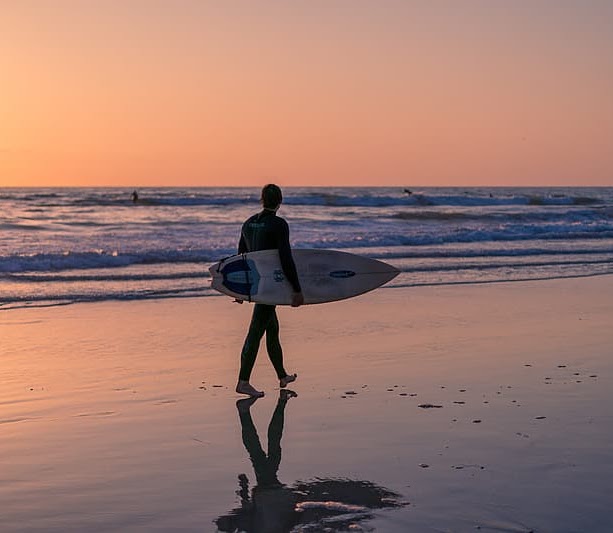 Man walking on the beach at sunset with surf board