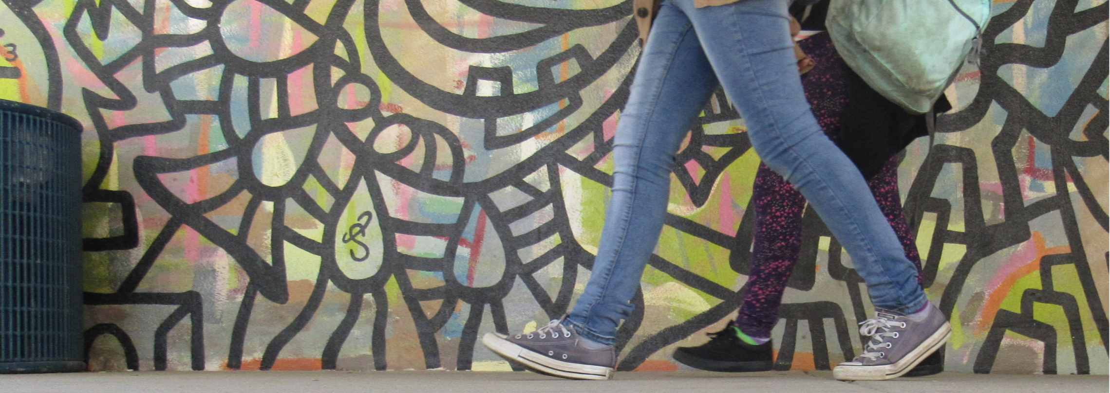 Two people walking in front of a mural