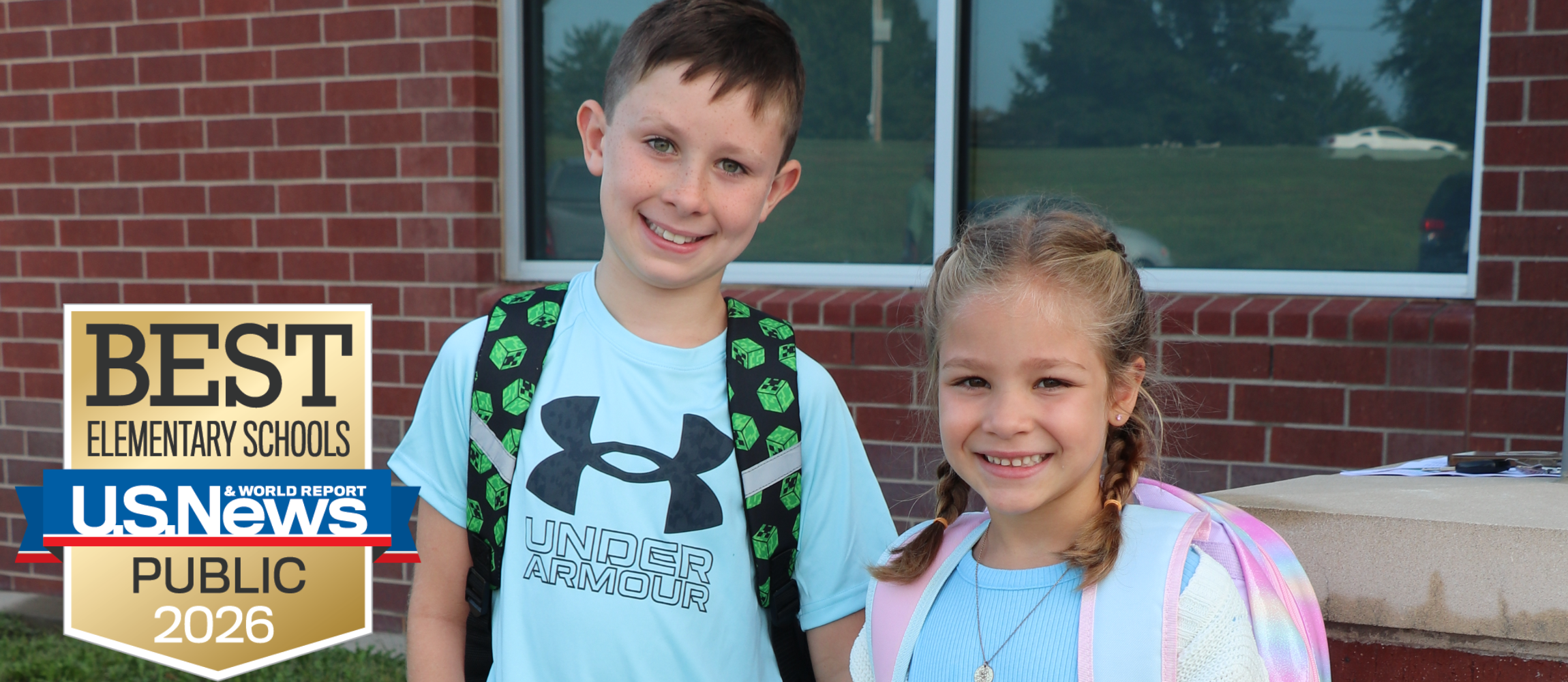 A brother and sister smile for a picture in front of the school building on the first day of school.