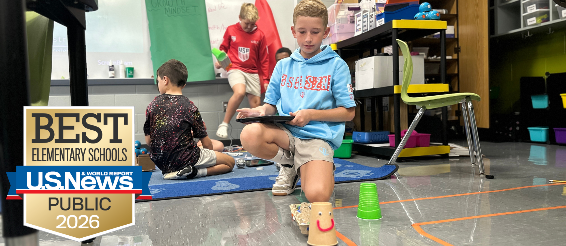 Student testing how many marbles the robot can haul. There is a logo for the US News and World Report Bes Elementary Schools logo in the bottom right.