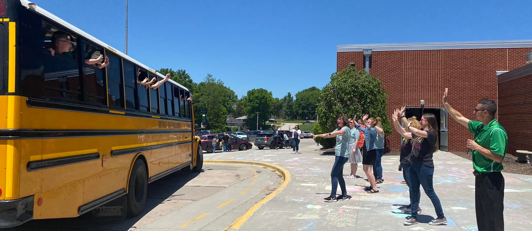 Teachers wave to students on bus on the last day of school