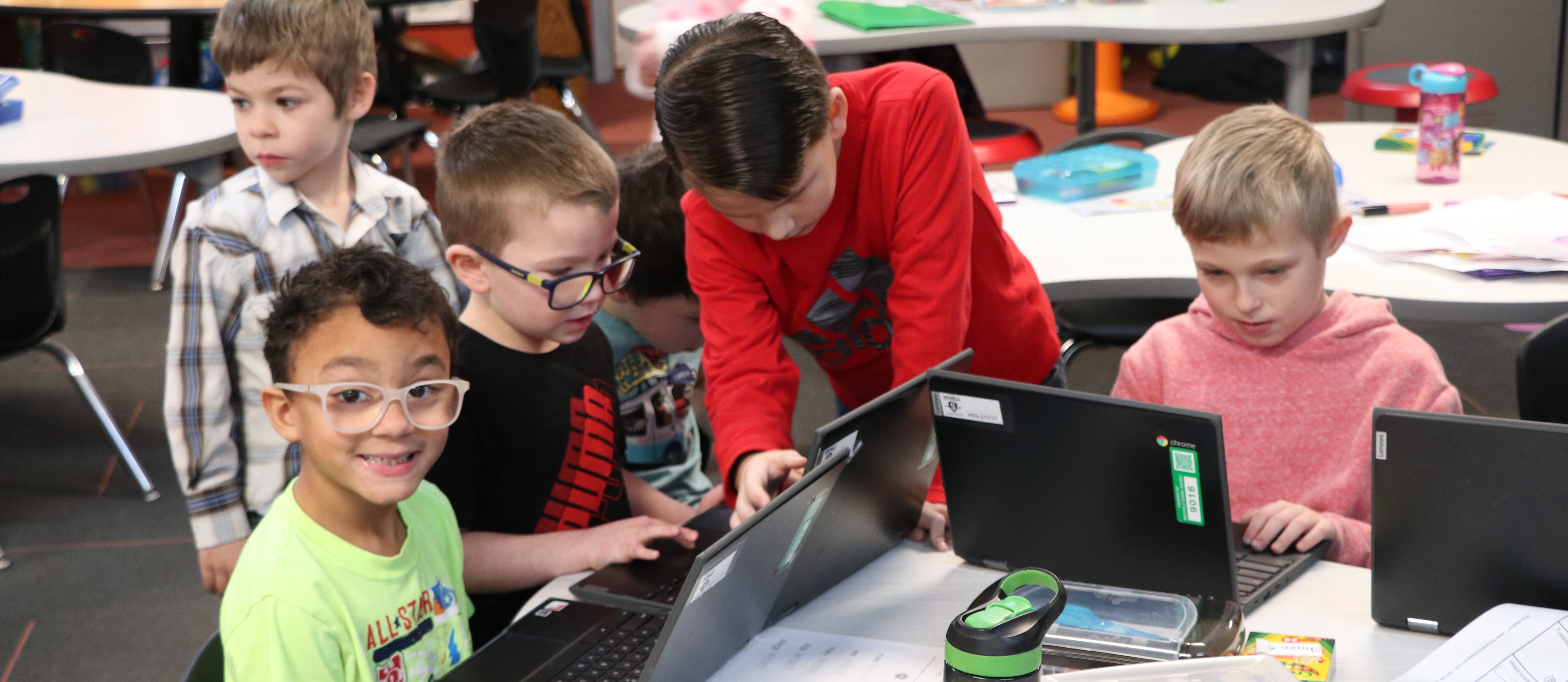 Boy smiles at camera while other boys look at a computer