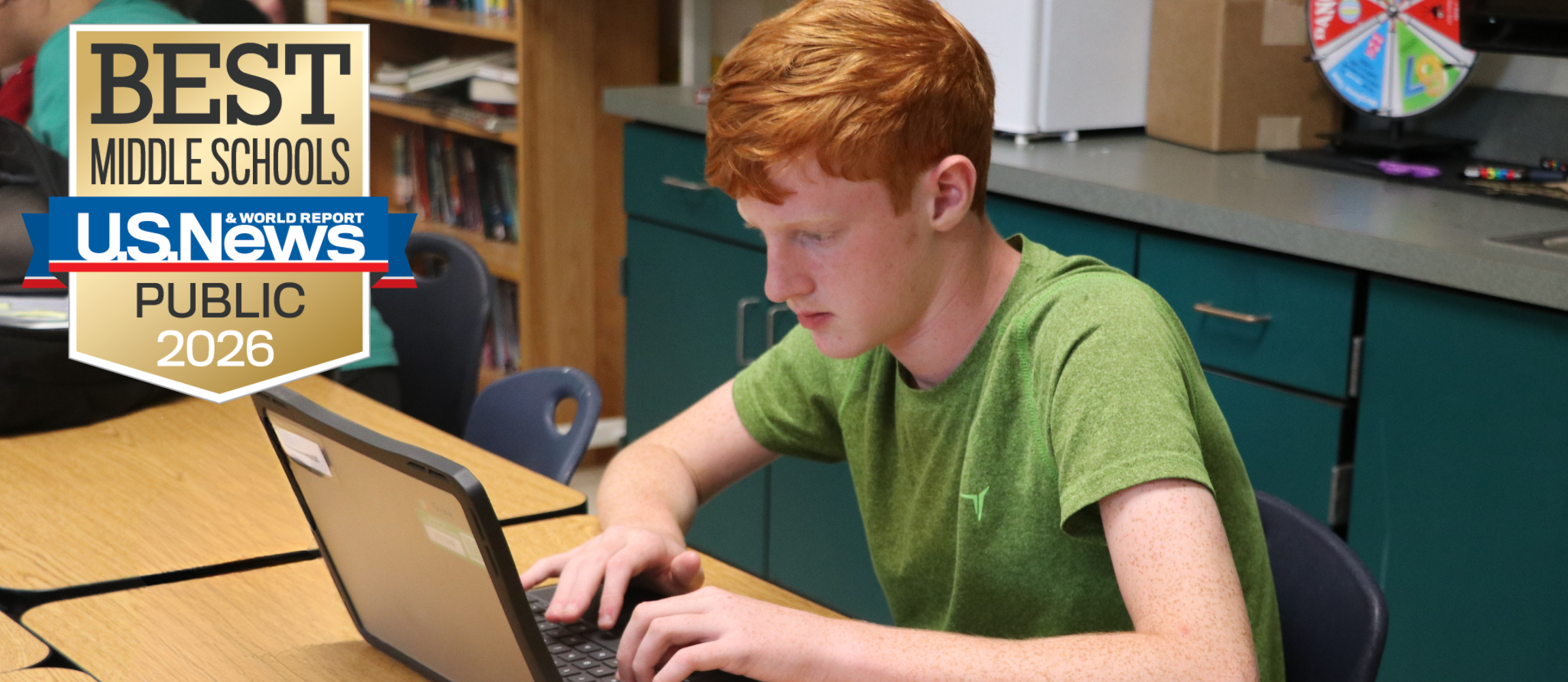 A boy is focused on his laptop computer sitting on the desk. There is a logo for the US News and World Report Best Middle Schools logo in the bottom right