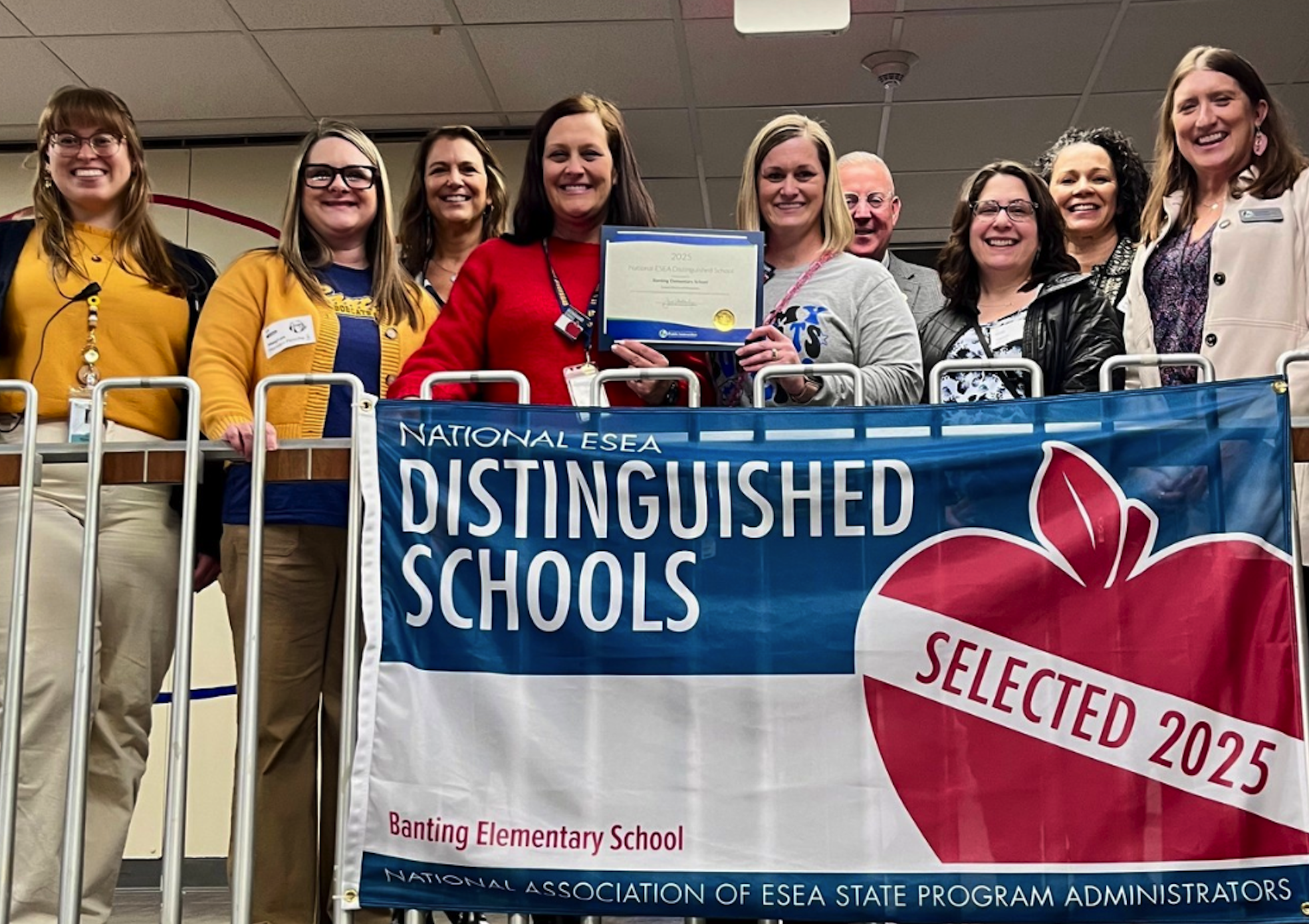 Adults stand on a balcony with a banner that reads "Distinguished Schools Selected 2025" and a red apple.