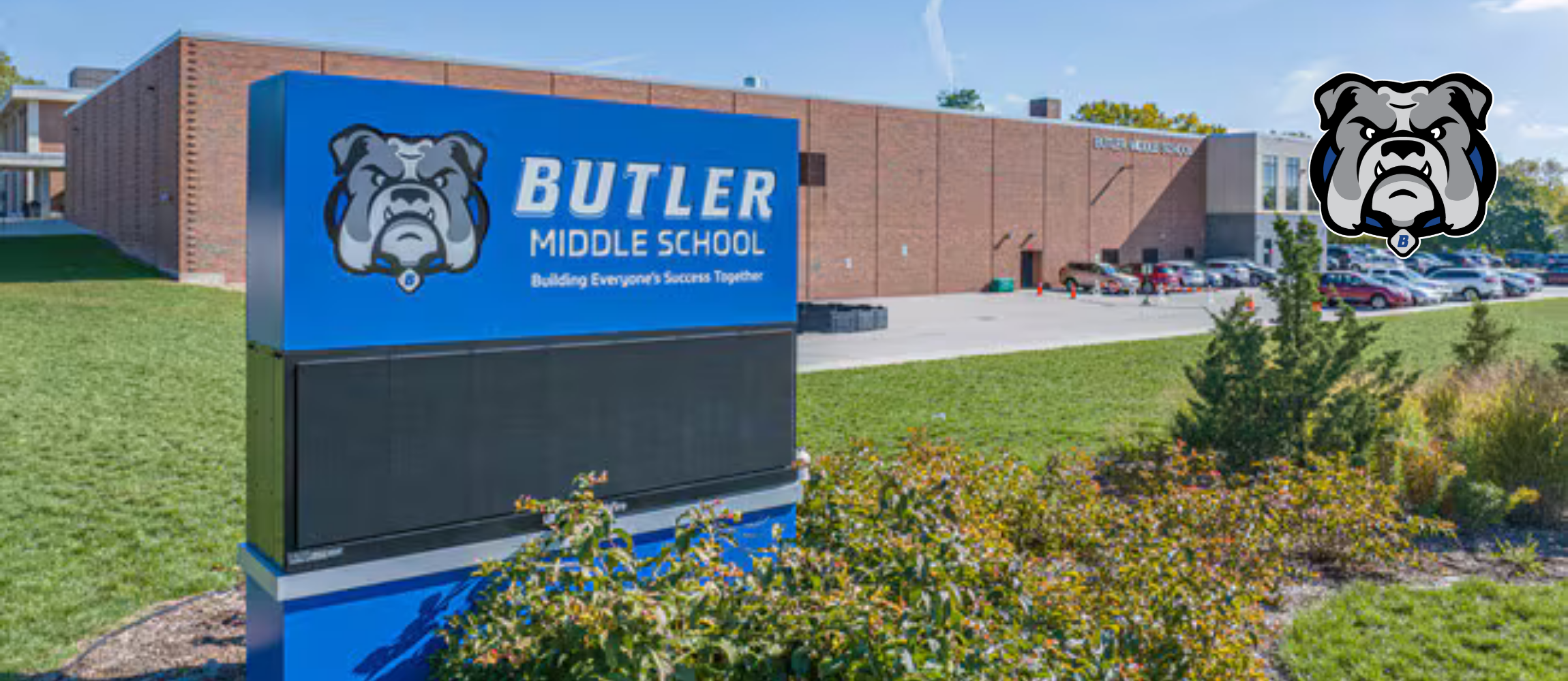 A blue sign with the words "BUTLER MIDDLE SCHOOL" and a bulldog logo stands in front of a brick building.