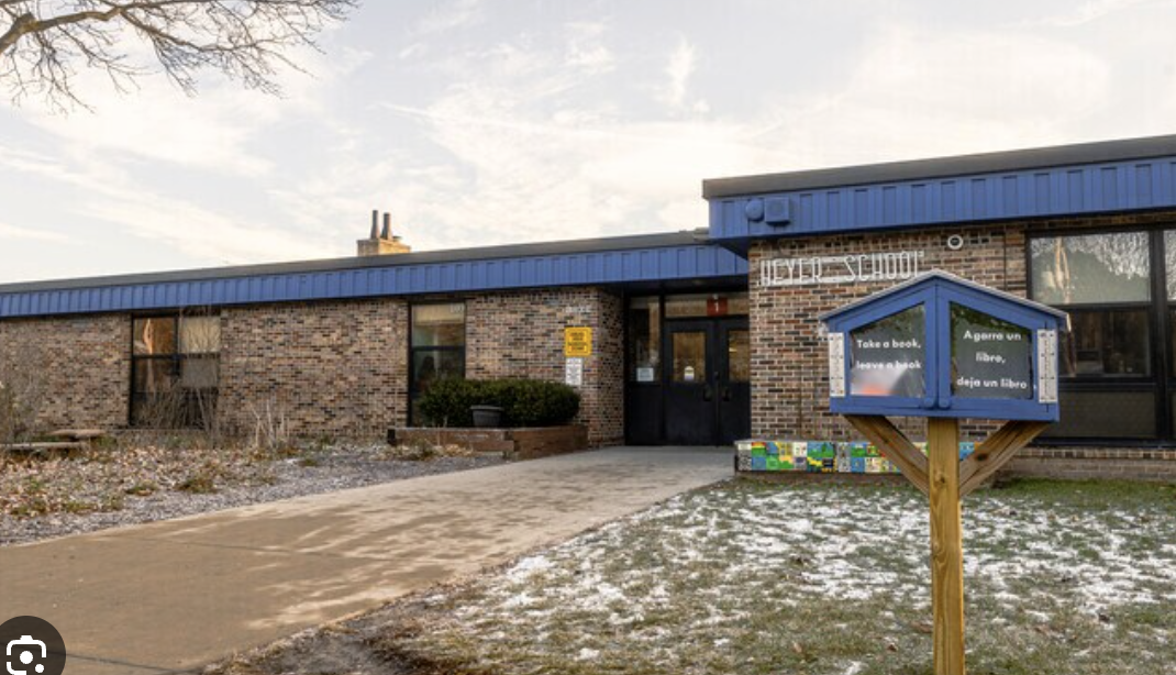 Exterior of a brick building with blue trim and glass doors. Snow-covered ground, a blue box, and a wooden post.