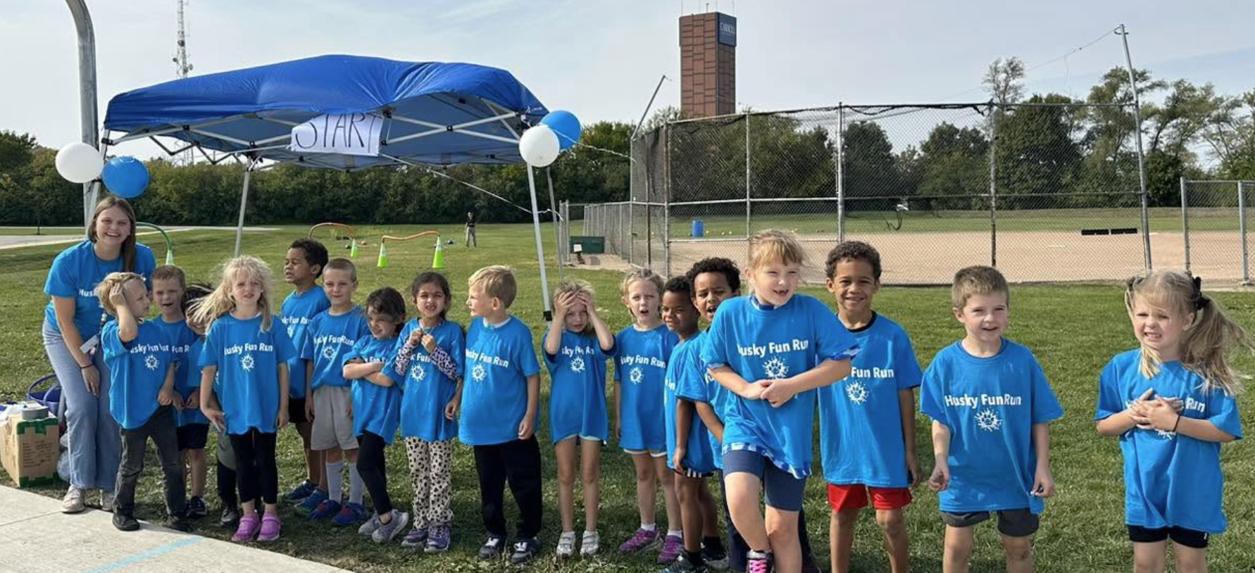 Children in blue shirts and sneakers pose for a photo under a blue tent with balloons.