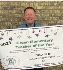 Chad Sanford smiling to the camera, holding a banner/recognition of teacher of the year