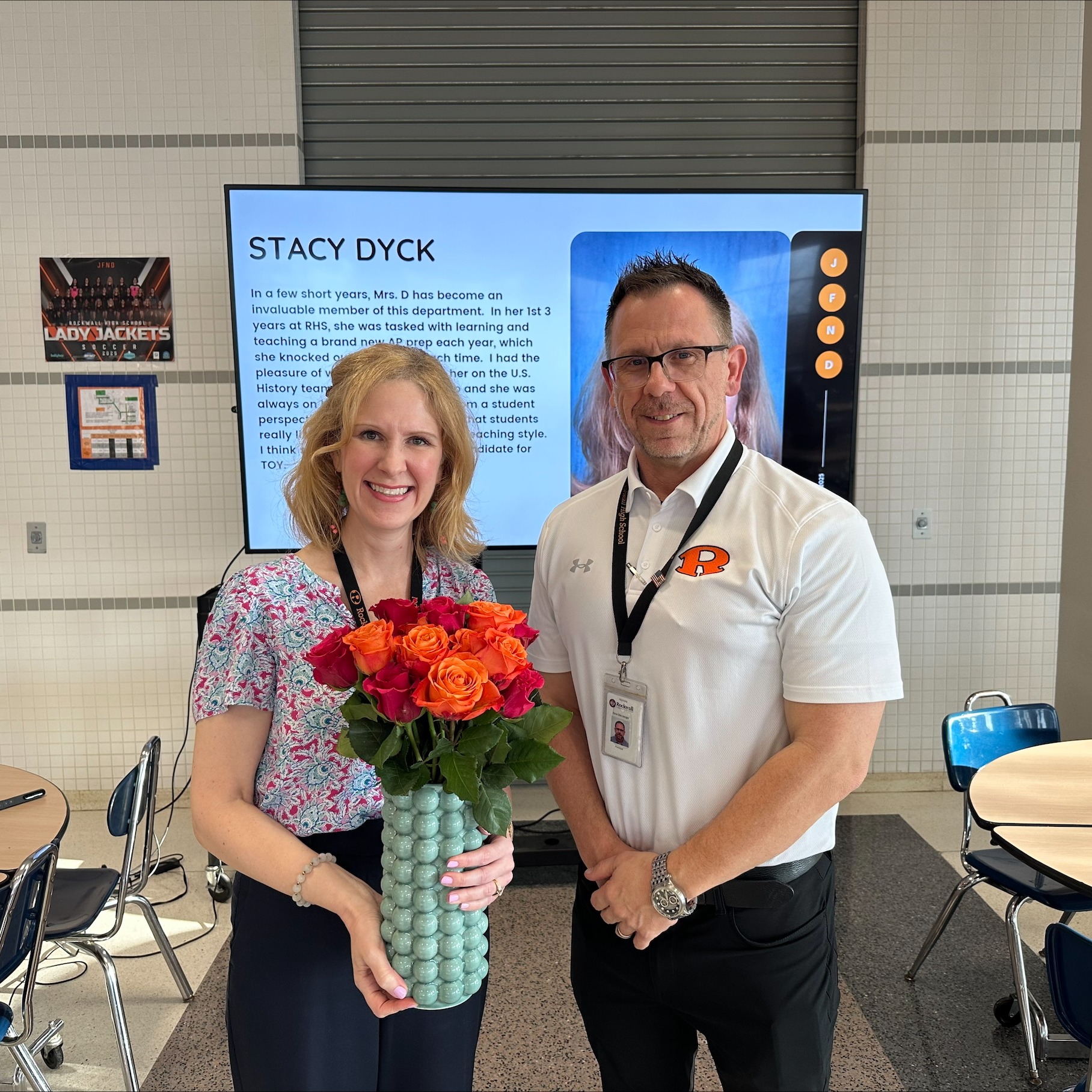 Stacy Dyck smiling holding flowers for receiving of teacher of the year, standing next to Dane Steinberger, RHS principal, smiling