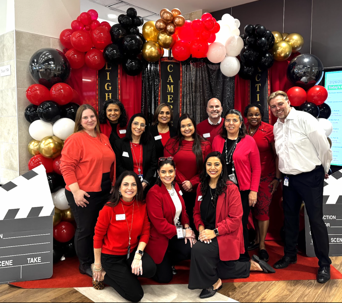 Team standing in front of a black and red background with a balloon frame