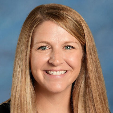 Woman with long blonde hair, wearing a black top, smiling at the camera against a blue background.