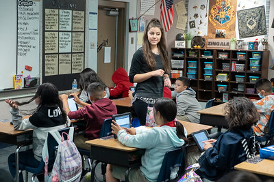 teacher standing in middle of classroom with students working in tablets