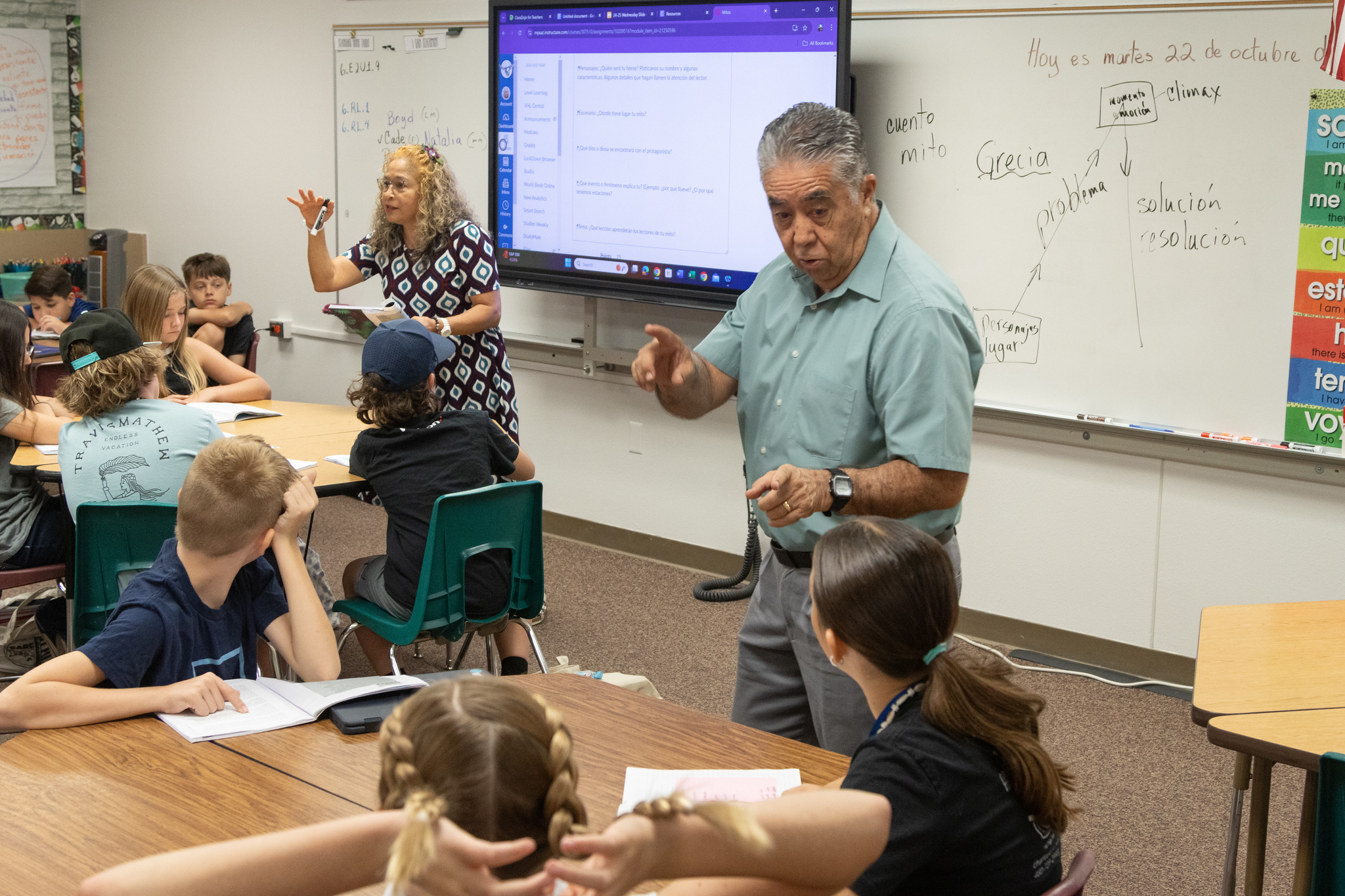 two teachers standing in front of classroom with students sitting at tables