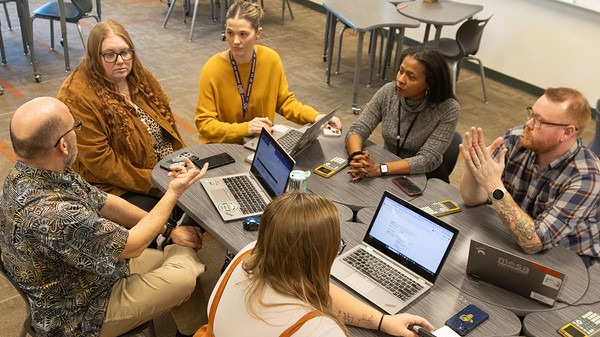 six teachers sitting around a table with laptops