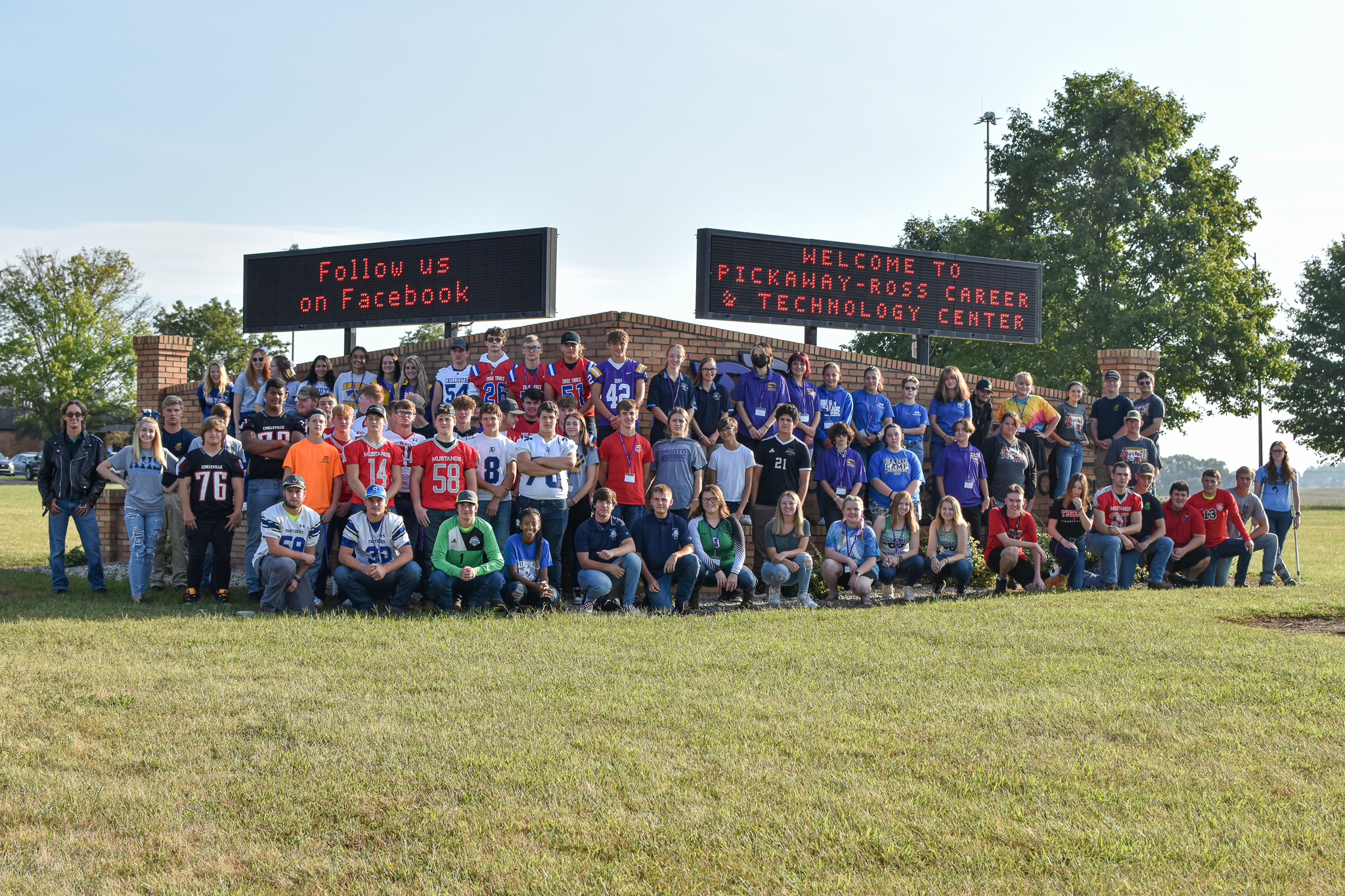 Students pose in front of the school sign in their sports jerseys. 