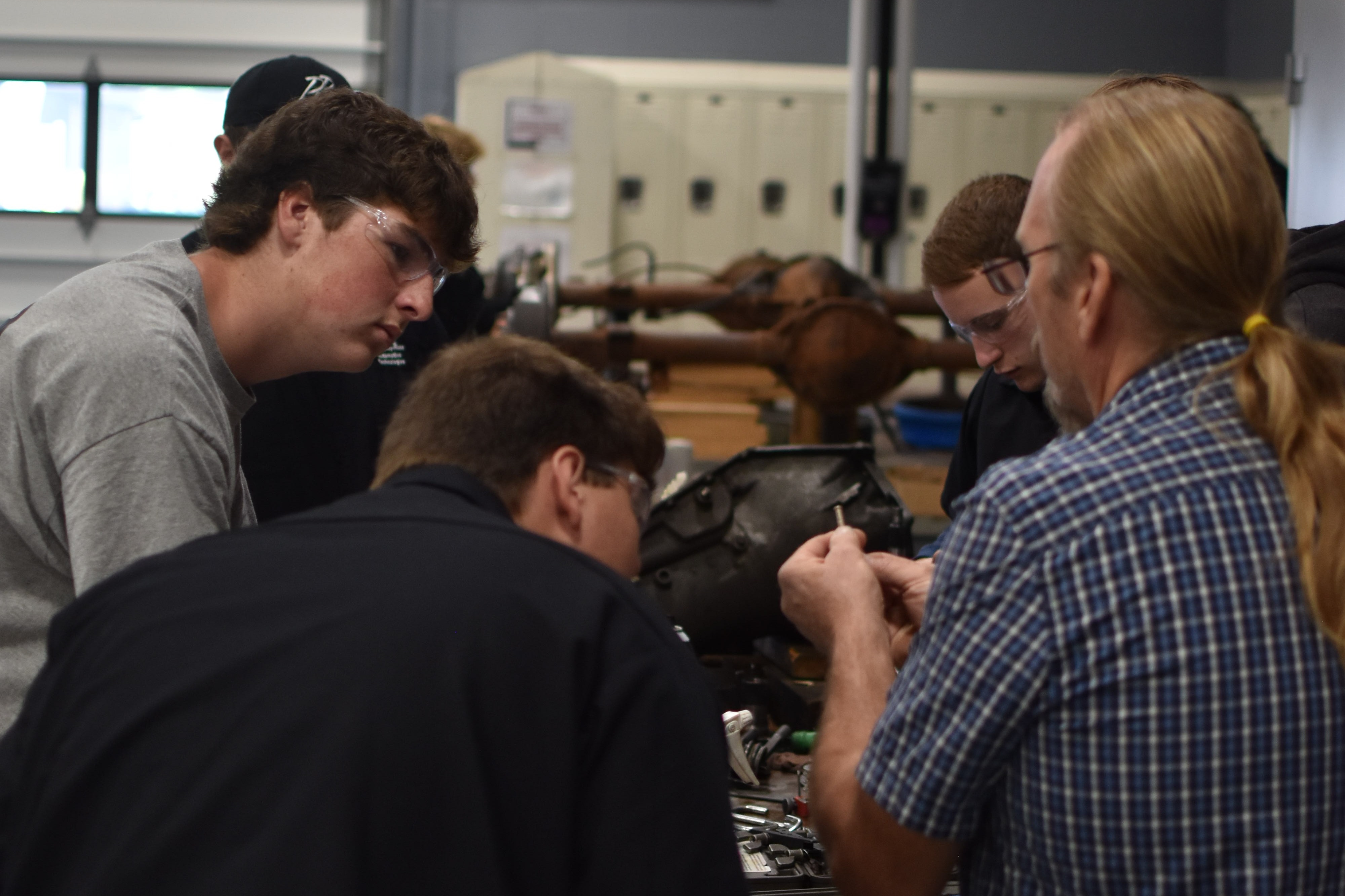 A group of people gathered in a workshop, looking at a machine with wires, possibly discussing its repair.