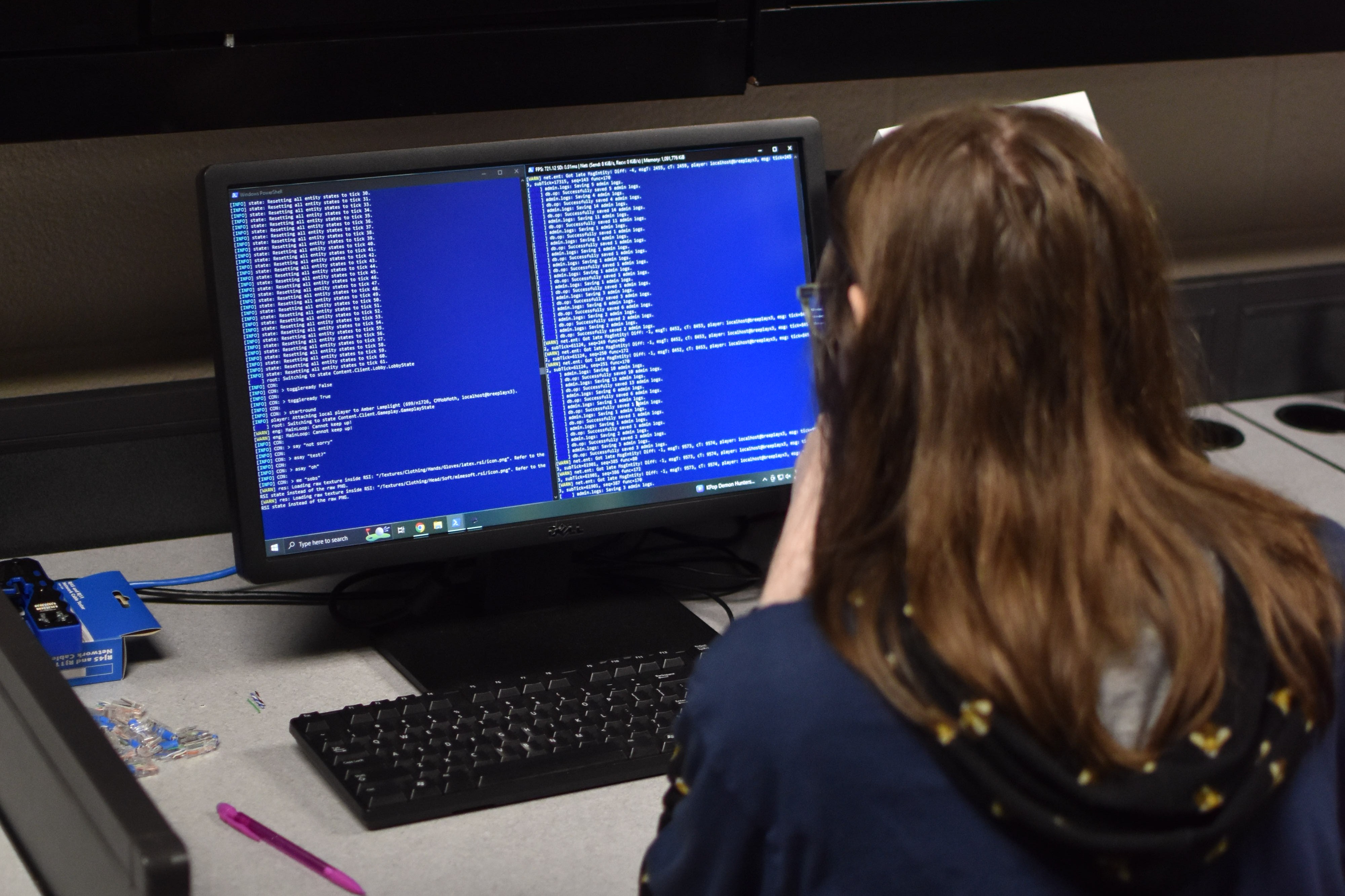 Person in a blue hoodie sits at a desk with a computer screen showing a blue graph.
