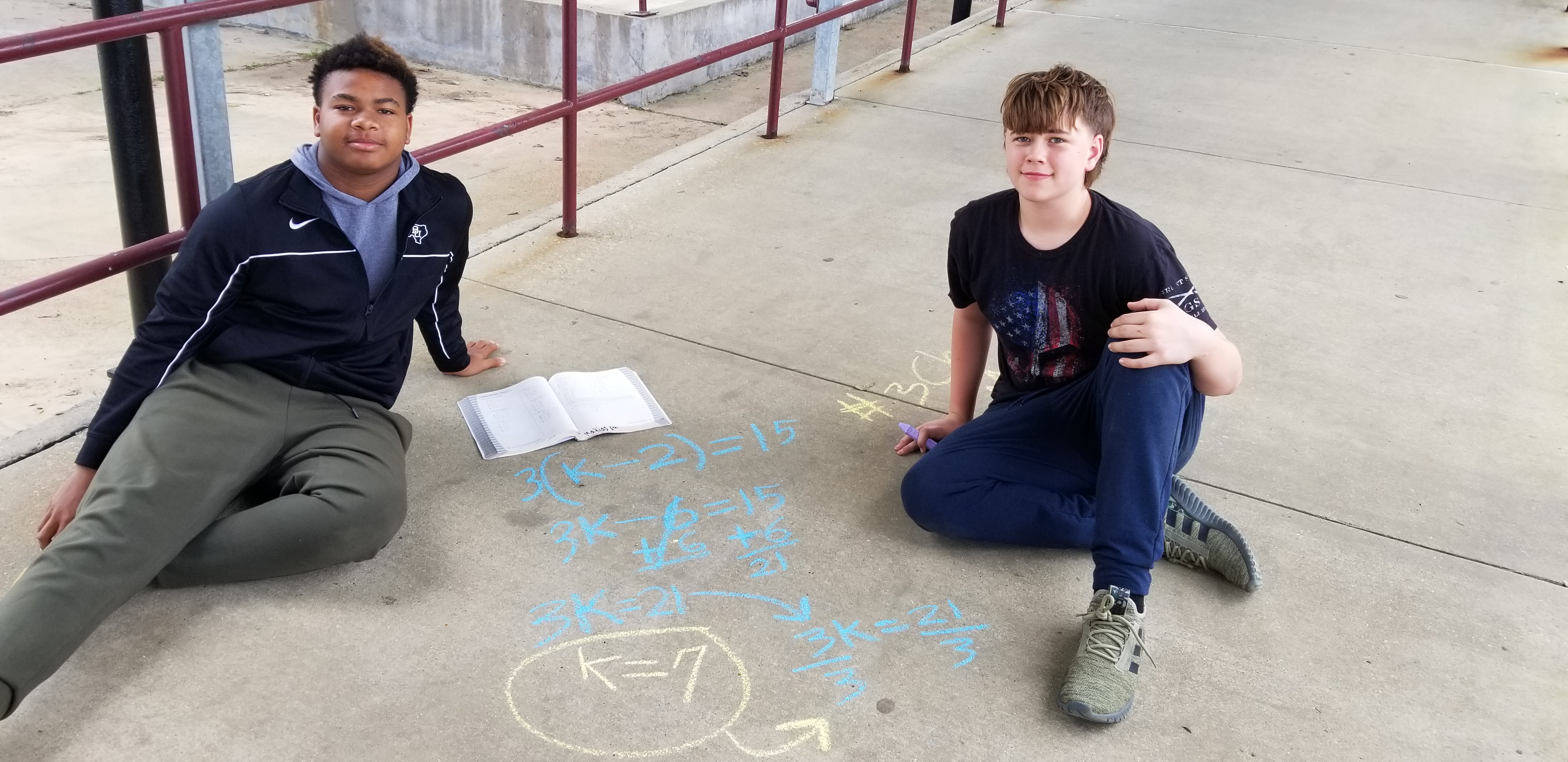 Two students outside working out math problems on concrete with chalk 