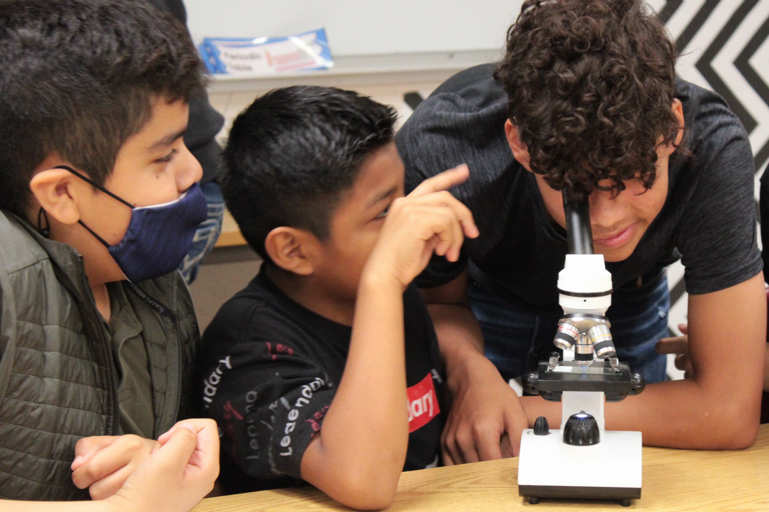 Three middle school students working on a project and one of them is looking into a microscope.