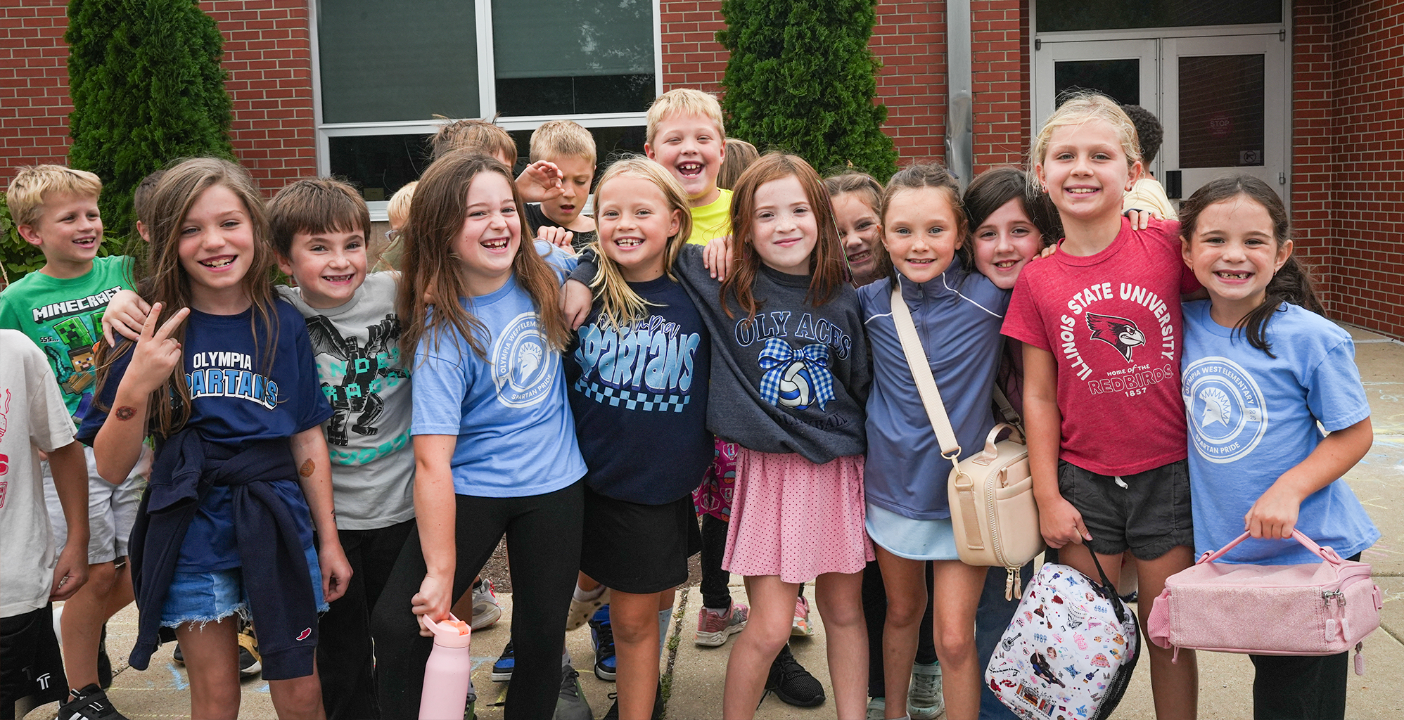 Group of students smiling on a sidewalk outside of a brick building