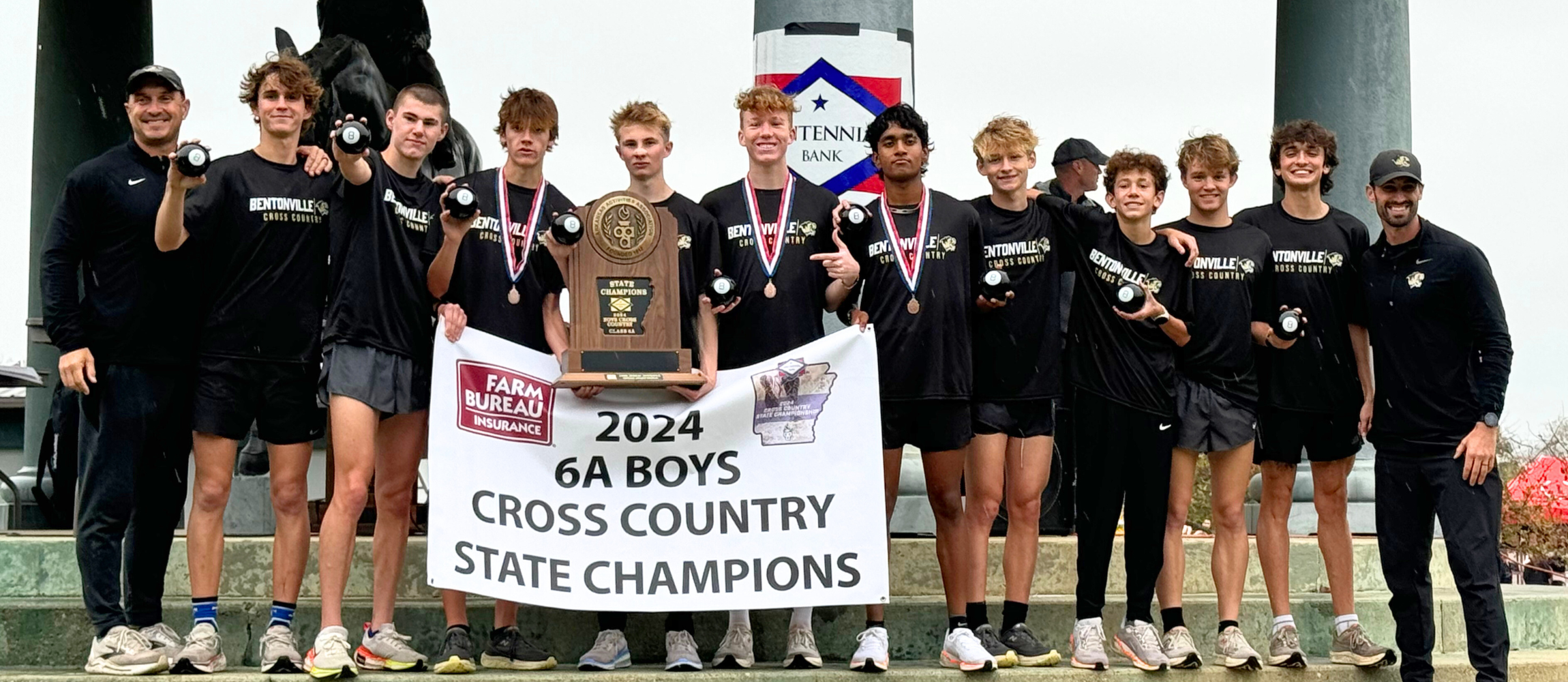 BWHS Cross Country boys posing on stairs in black t-shirts with a State Champion sign and Wolverine logo on top of image