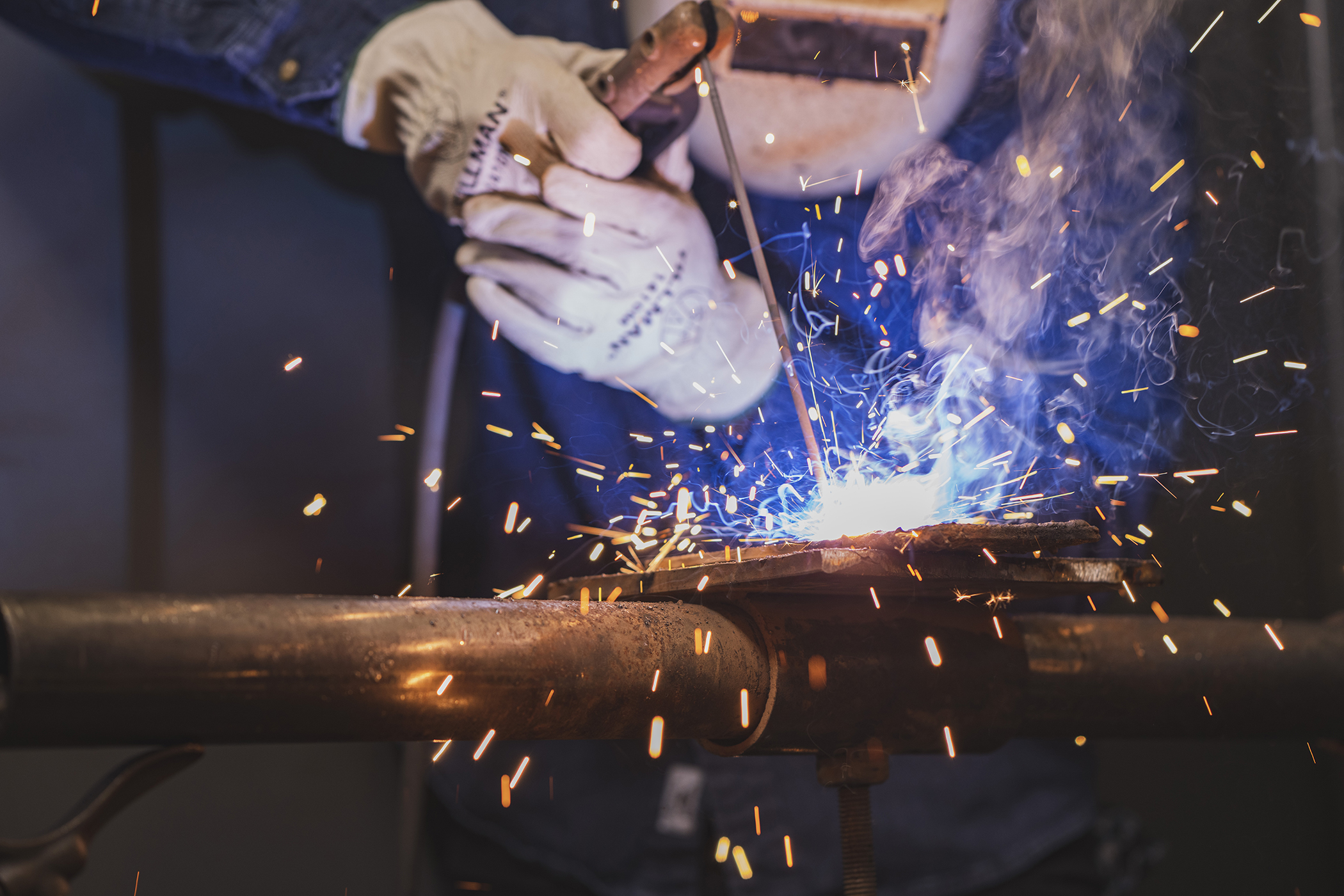 Person in welding helmet and gloves welding metal.  