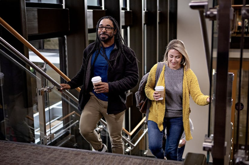 two adult students walking up office staircase with coffee