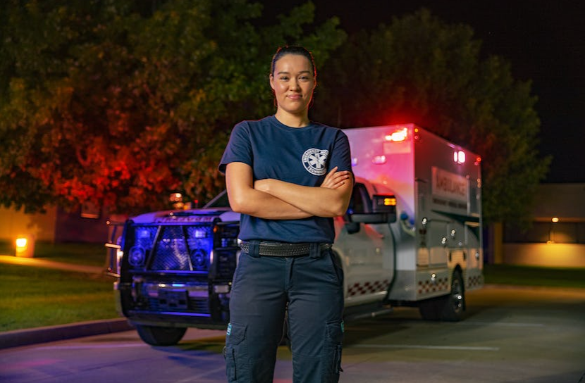 emt posing for picture outside with ambulance in the background flashing red lights