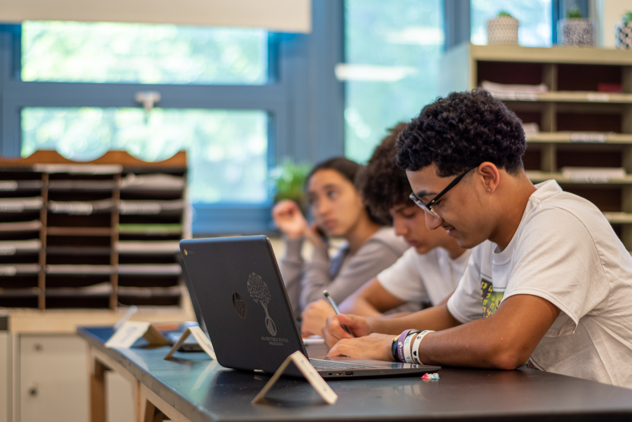three students seated at classroom work table with one student working on a laptop 