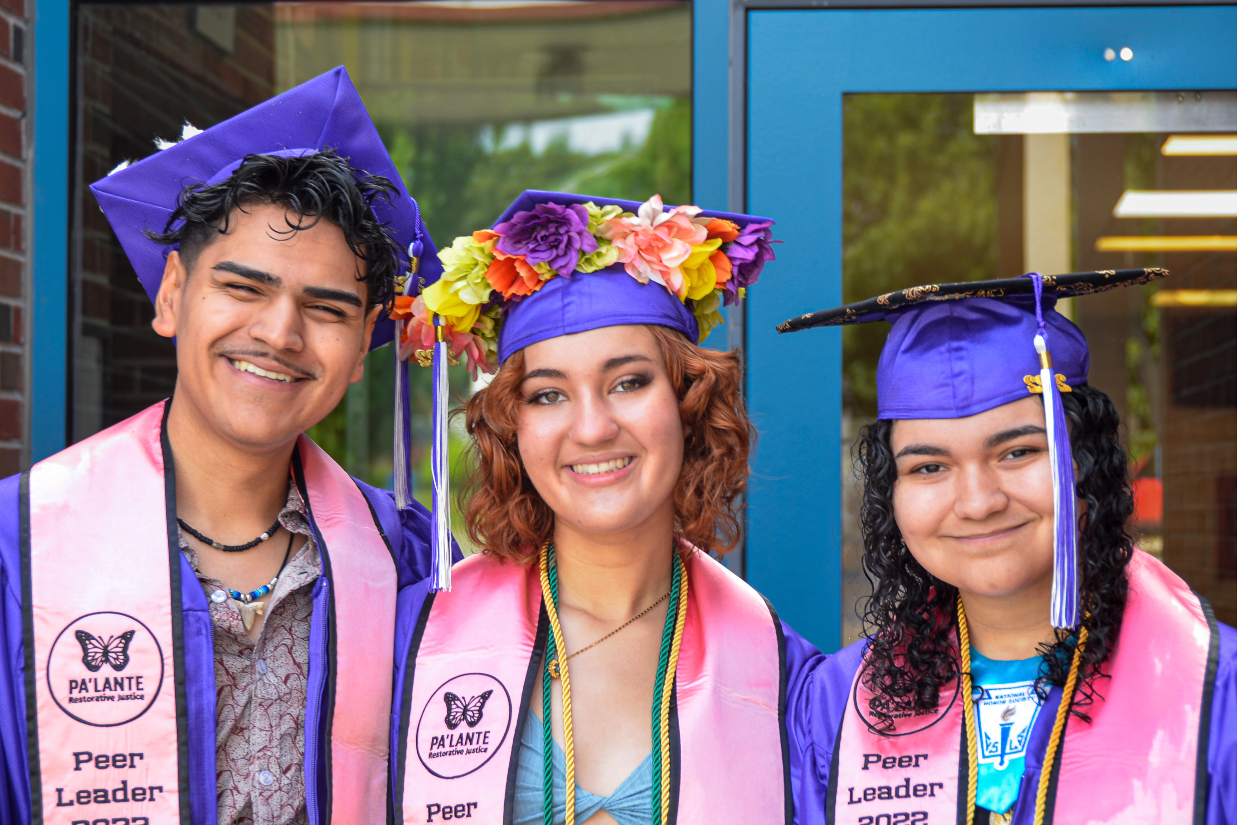 three high school students smiling in their caps and gowns on graduation day 