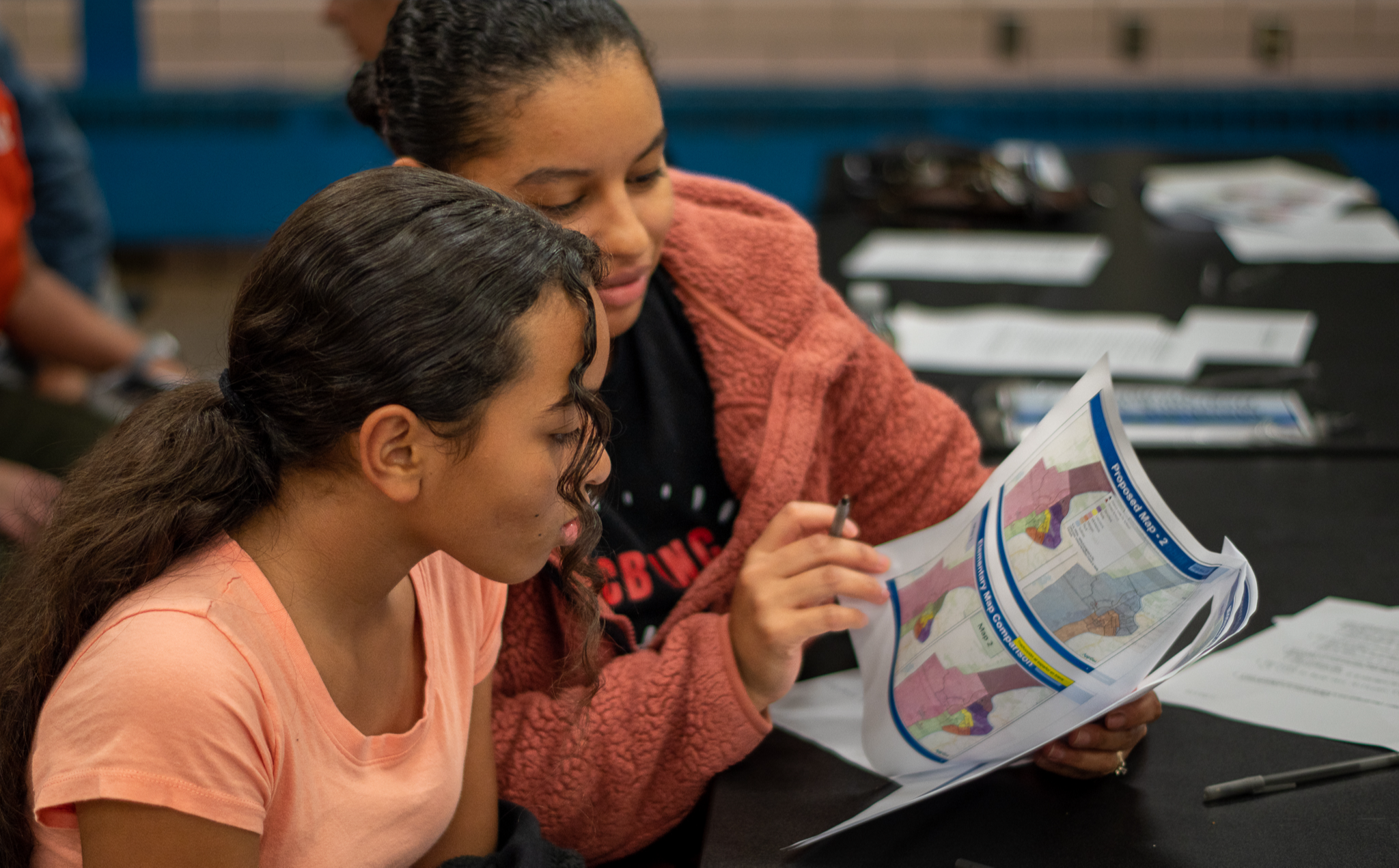 Student and parent at a district meeting looking into a packet of papers prominently showing maps of the City of Holyoke. 
