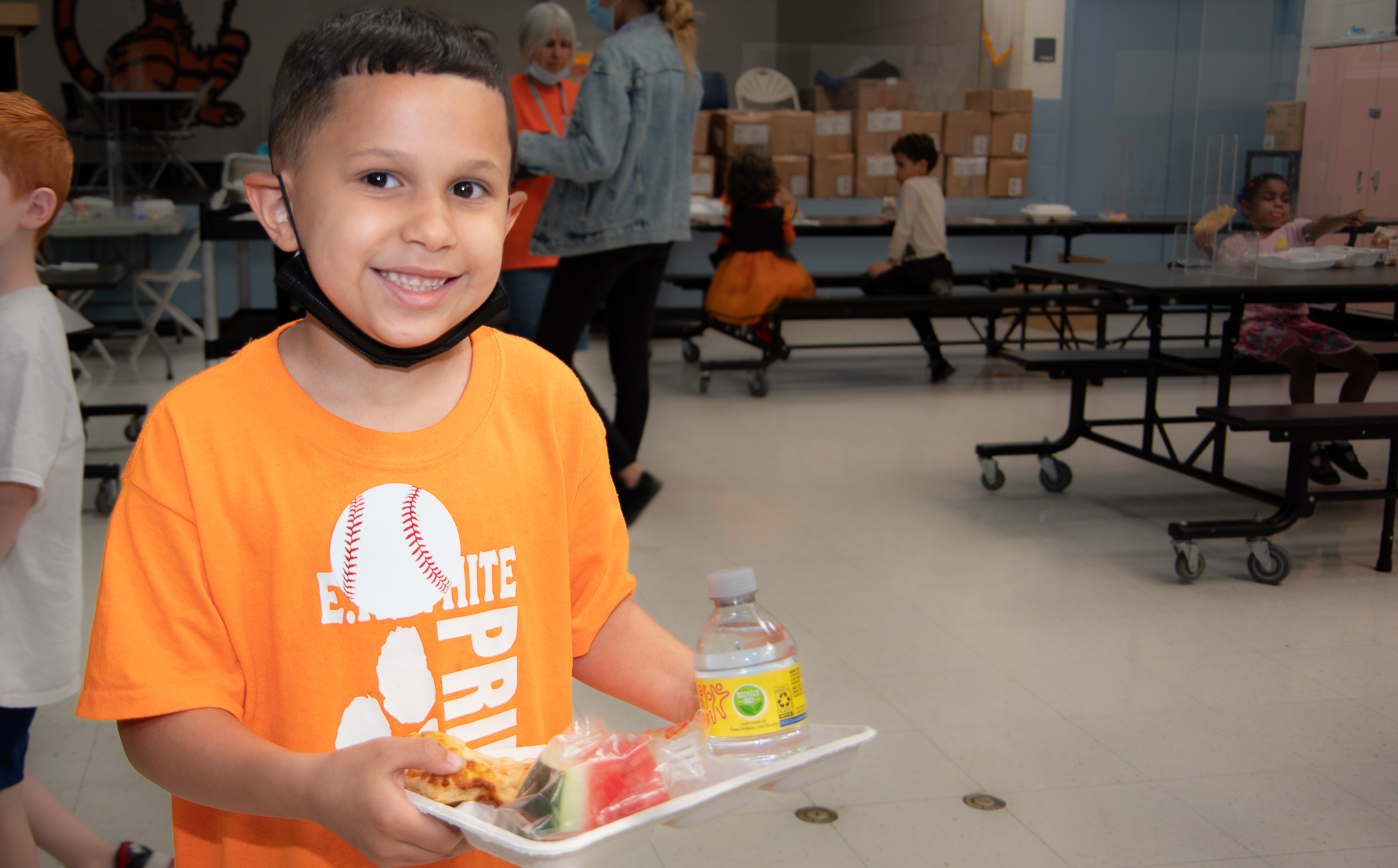 Student smiling for the camera at a school cafeteria holding a food tray with lunch.