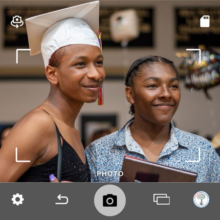 Student wearing their graduation cap next to young woman posing for a picture during graduation ceremony.