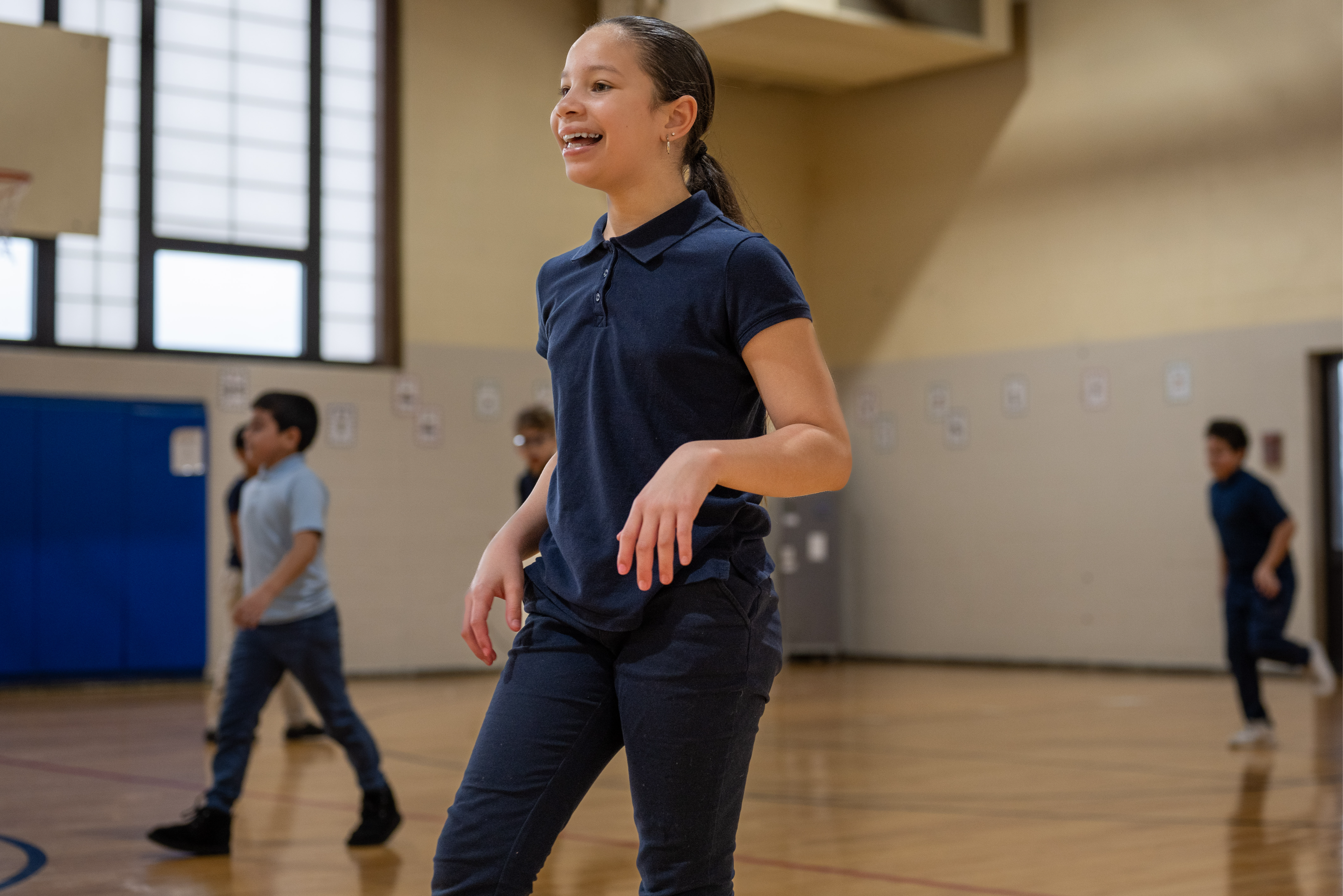 A smiling student in gym class waiting for her turn to get the ball.