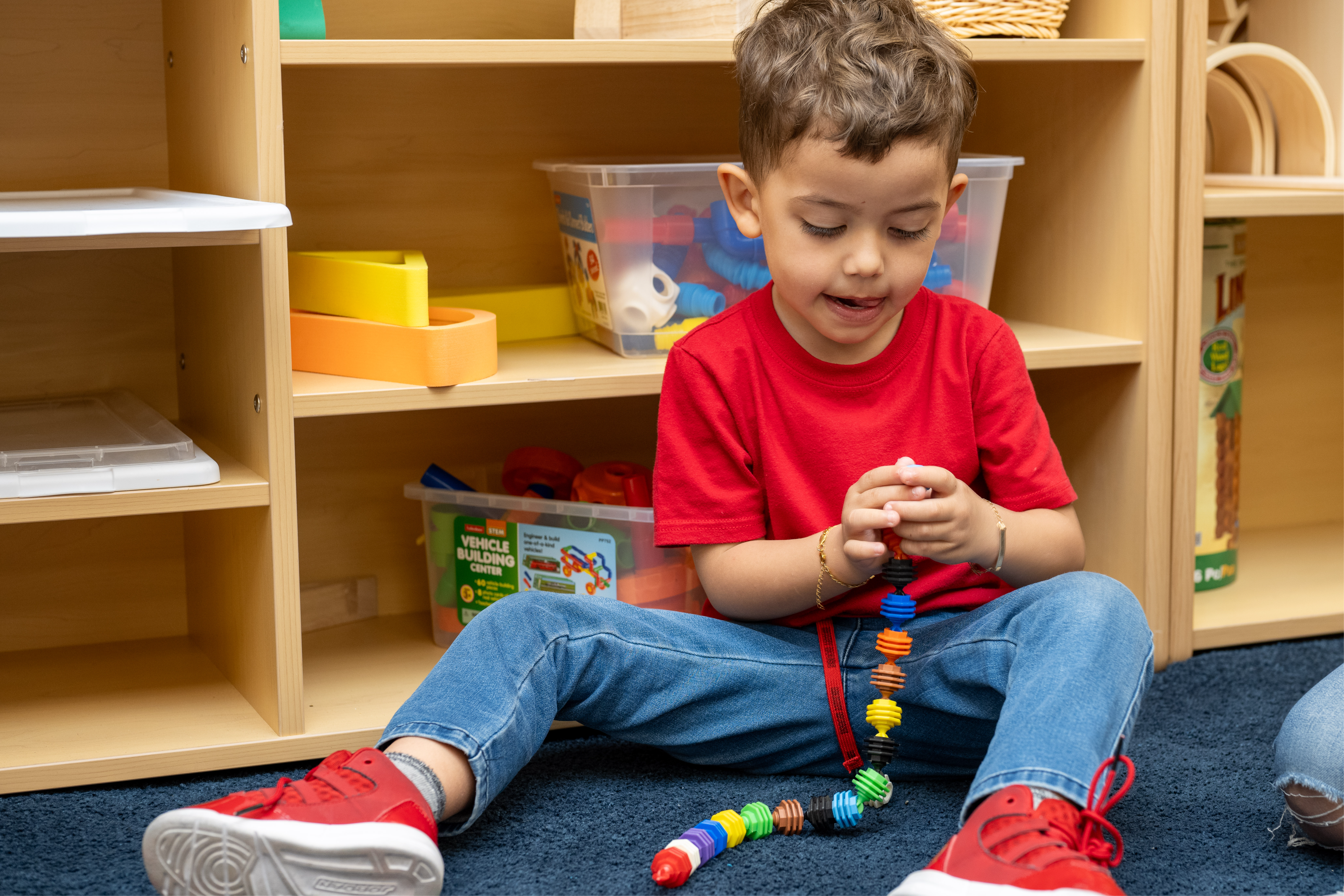 A young student sitting down on the floor creating a string. 