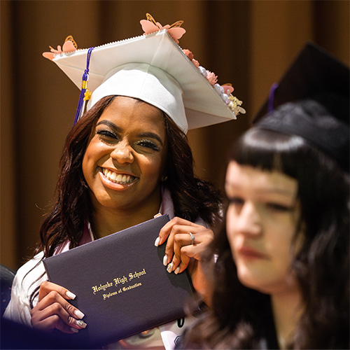 A smiling student holding her Holyoke High School diploma of graduation 