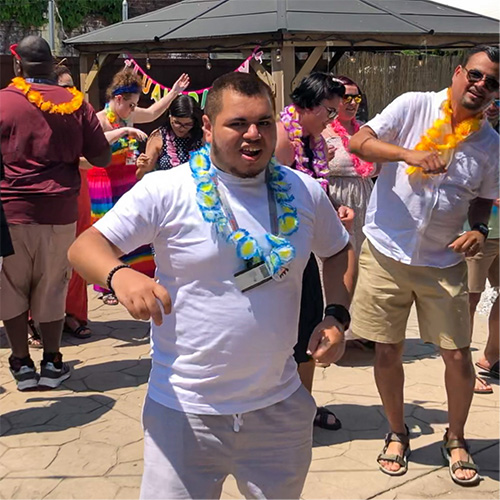 A student captured smiling at the camera while other staff and students in the background dance.