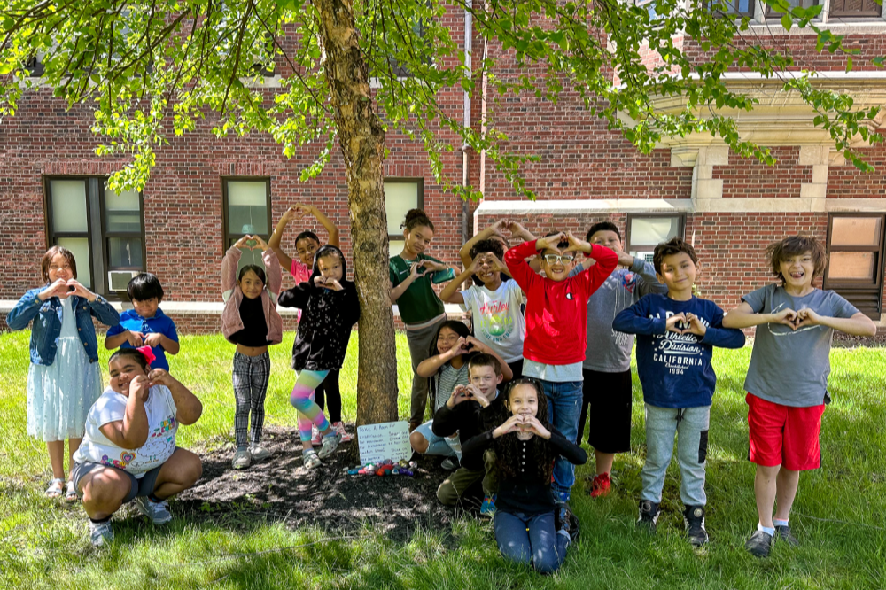 A group of elementary school students making heart shapes outside.