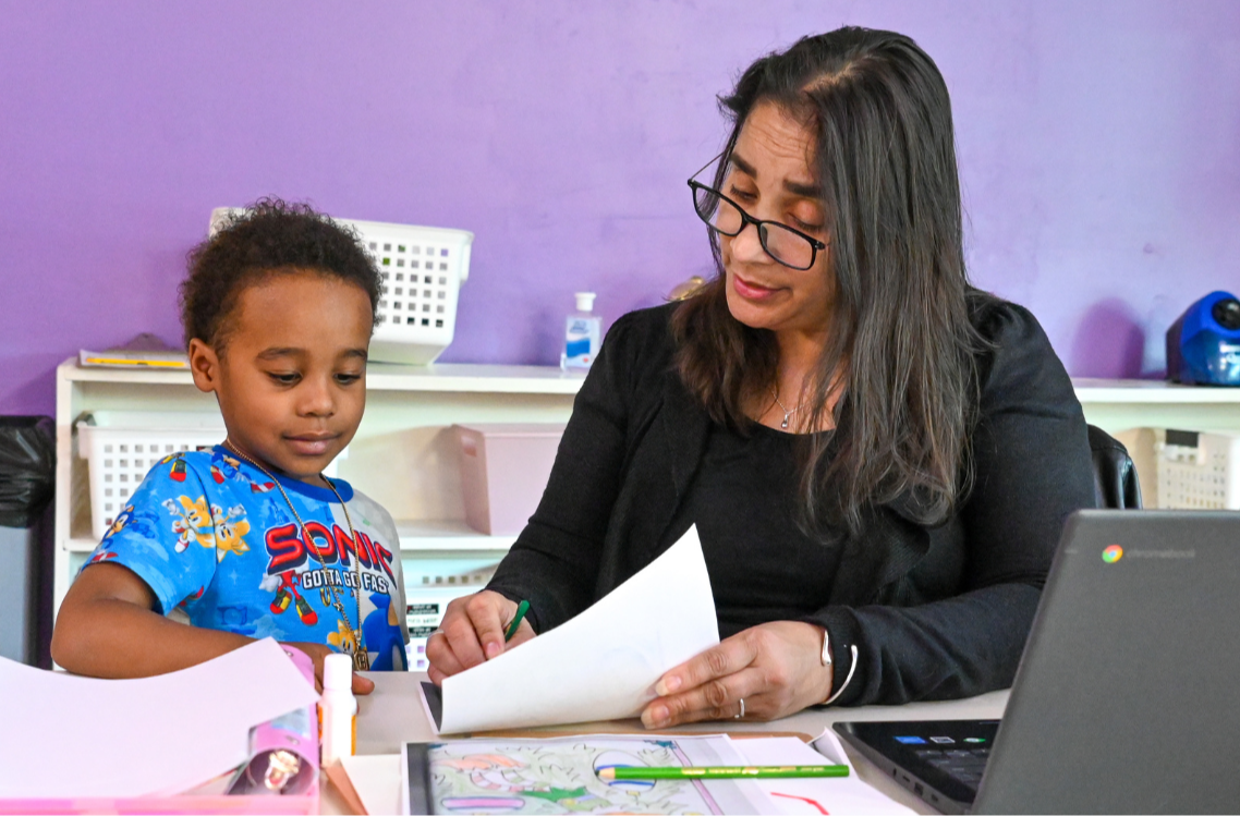 A teacher helping a student paint her hand for hand painting activity.