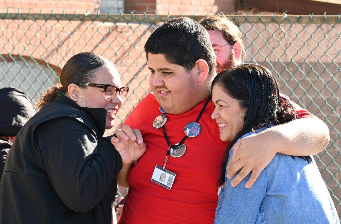 A Transitions Academy student laughs with two coaches outside in the sun