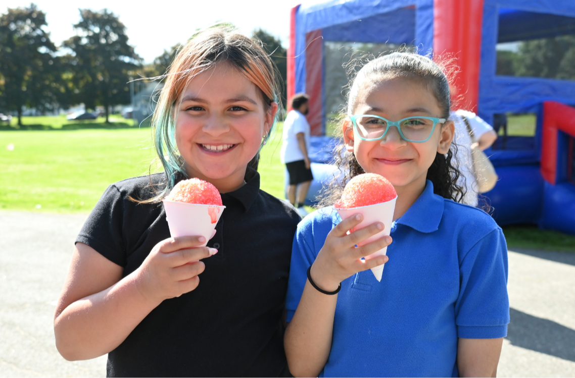 Two students smile while enjoying snow cones during a community event