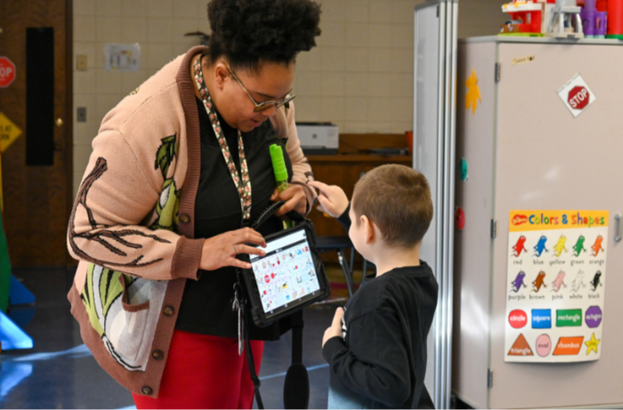 A staff member holds a talking board for a student