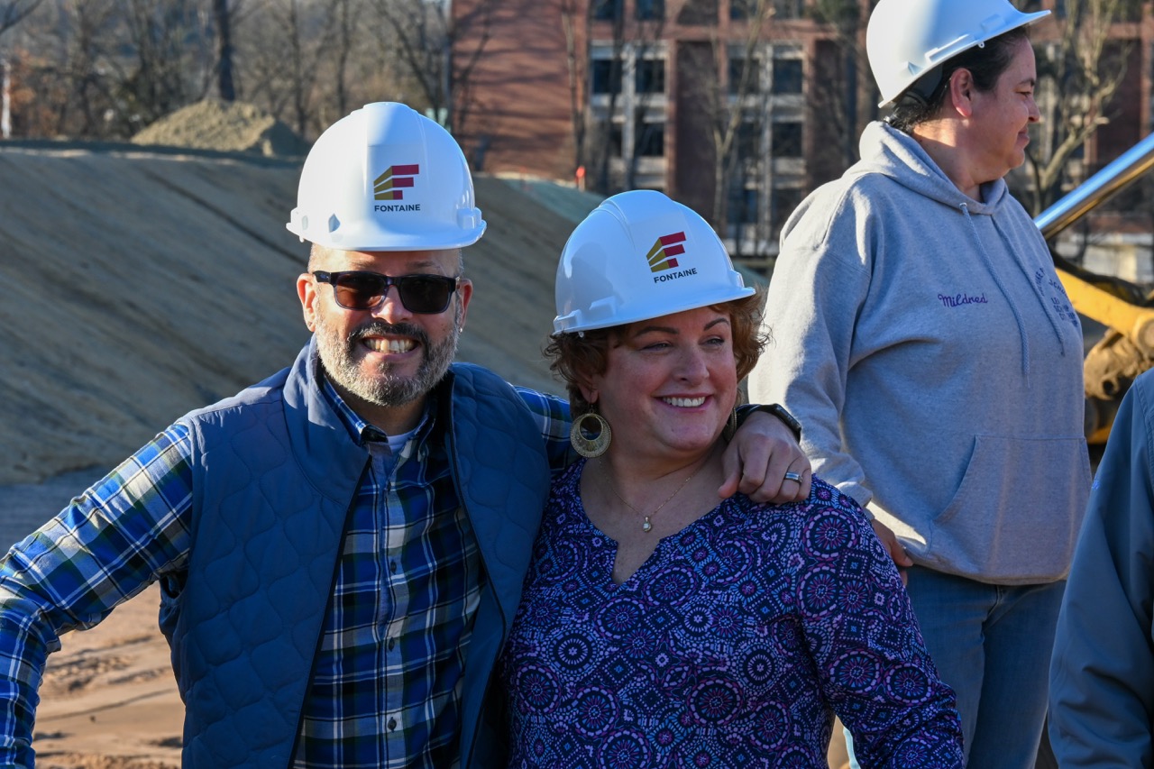 Two people in hardhats hug and smile