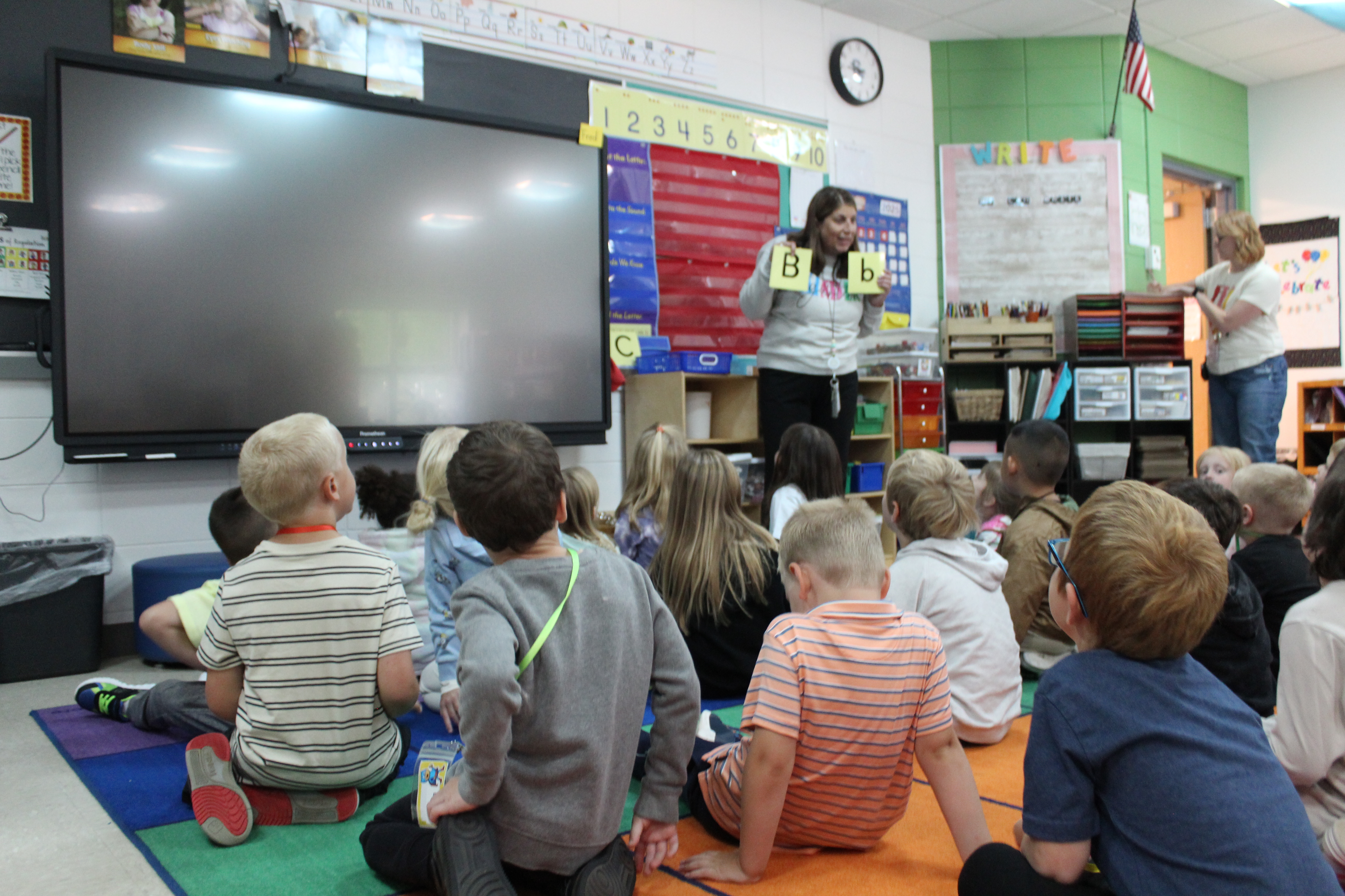 teacher holding up letters with students looking on