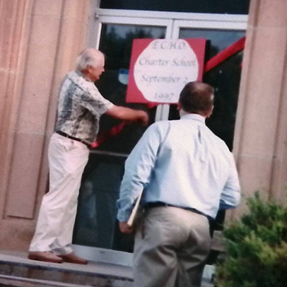 two men cut a red ribbon on a school door