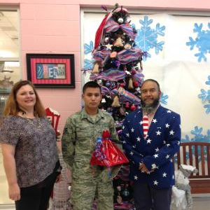 Staff members posing with a military serviceman in front of a Christmas tree