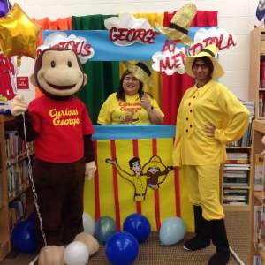 Two staff members dressed as the Man in the Yellow Hat posing with a life size Curious George statue