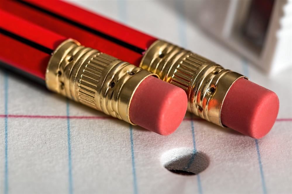 Two pencils, with the erasers in focus, resting on top of a page of notebook paper